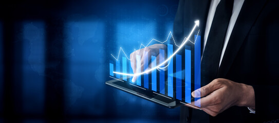 A businessman in a suit interacts with a digital tablet displaying growth charts and financial data. The blue background highlights the technological aspect of modern finance and analytics. Impute