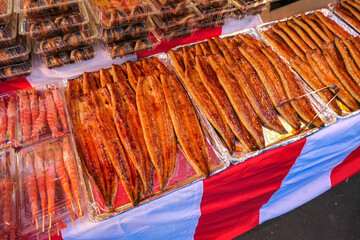 Delicious-looking glazed and grilled eel, or unagi, is displayed on foil trays at a bustling...
