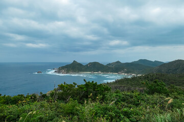 From a high viewpoint, a rugged coastline with lush green mountains and dramatic cliffs meets  deep...