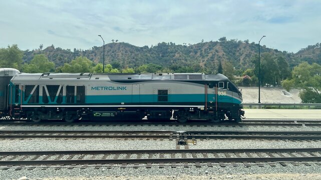 LOS ANGELES, CA, AUG 28, 2025: Metrolink diesel locomotive with classic teal and gray livery, hills and trees in background, concrete flood channel visible