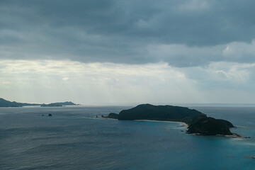 Divine rays of sunlight pierce through dramatic, heavy cloud cover to illuminate a patch of vast...