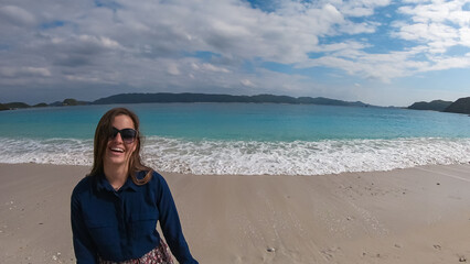 A close-up, wide-angle shot of a joyful young woman with sunglasses laughing happily on the beach....