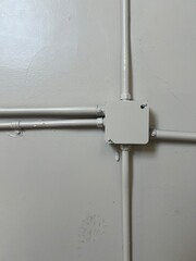 Simple electrical junction box mounted on a grey-white wall with conduit pipes running horizontally, showing basic industrial or commercial electrical infrastructure installation