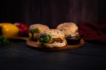 Tasty grilled or crispy beef or chicken burger served on pieces of brown wood on a rustic wooden table. Big double cheddar cheese burger with crispy chicken and capsicum.