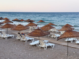 Beach with straw umbrellas and sun loungers by the sea. Summer vacation, relaxation and coastal...
