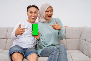A very joyful couple happily poses together with a smartphone that features a green screen