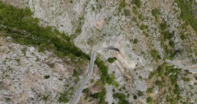 Aerial view of a winding road cutting through the rugged, rocky mountains, with lush green vegetation clinging to the steep slopes, Anversa degli Abruzzi, Abruzzo, Italy.