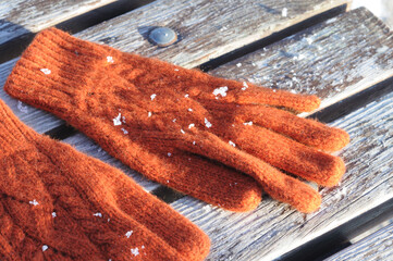 Orange woolen gloves on a wooden bench covered in snow. Winter clothing.