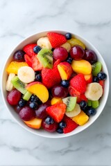 A vibrant mix of fresh fruits including strawberries, blueberries, bananas, peaches, and kiwi is elegantly arranged in a white bowl on a marble countertop, creating a refreshing treat