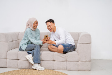 Two friends laughing together on a cozy sofa, sharing a smartphone and making memories