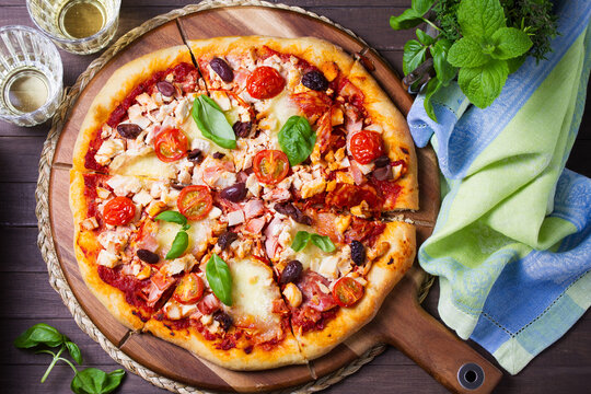 Delicious pizza served on wooden pizza board on brown background. View from above, top studio shot