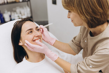 Cosmetologist drawing marks on woman's face before cosmetic injections