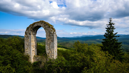 Ancient stone archway ruin in a lush green landscape with rolling hills and clouds