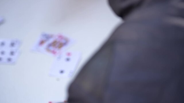Scattered playing cards on a white table surface with a blurred human back silhouette in close-up