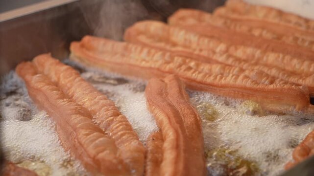 Golden crispy traditional Chinese youtiao being deep fried in hot oil