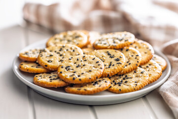 Crispy round salted crackers with sesame seeds on plate on white table.