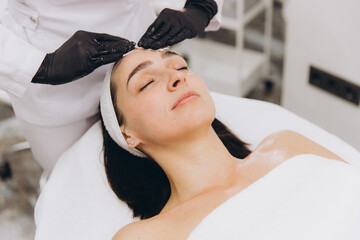 Beautician Applying Cream on Woman's Forehead for Facial Treatment