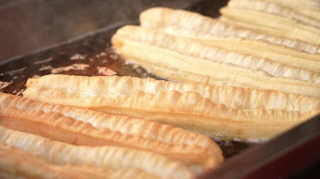 Freshly fried golden crispy youtiao being cooked in hot oil in a wok