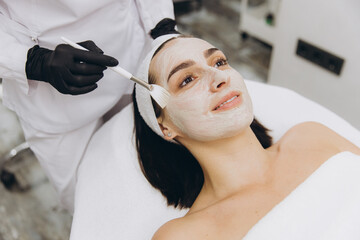 Beautician applying a facial mask to a young woman