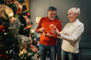 Senior couple decorating christmas tree with red ornaments