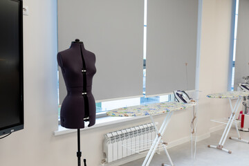 Naklejka na ściany i meble Tailor's dummy and sewing equipment in a bright workspace. Tailor's dummy, ironing boards in a modern sewing workshop. Photo