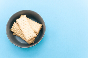 ciotola di colore scuro con biscotti secchi privi di zuccheri per una  sana prima colazione o spuntino, superfice di colore azzurro con vista da sopra