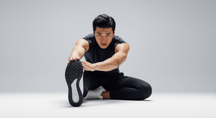 Obraz premium Muscular Asian man stretching his leg before a fitness workout. Fit athlete doing a flexibility exercise on a white background with copy space.