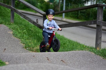 Young boy wearing helmet rides red balance bike on outdoor pump track with high curbs. Exciting...