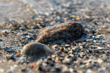Close-up view of smooth stones and pebbles on a sandy beach, with gentle waves lapping at the shore, creating a serene coastal atmosphere and natural beauty