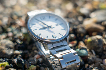 Silver wristwatch with a white dial resting on a bed of pebbles, showcasing intricate details and...