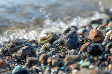 Colorful pebbles and smooth stones scattered along the shoreline, with gentle waves lapping at the water's edge, creating a serene coastal atmosphere and natural beauty