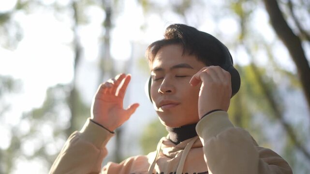 Young man outdoors closing eyes while adjusting headphones in a calm pose