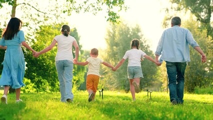 Family, mom dad son daughter run together, happy childhood, free people. Mom dad kids holding hands running, playing, having fun in city park in summer. Slow motion. Happy family. Family game concept
