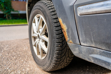 Close-up of rusty corrosion on car fender above the wheel, showing vehicle aging, metal damage, and...