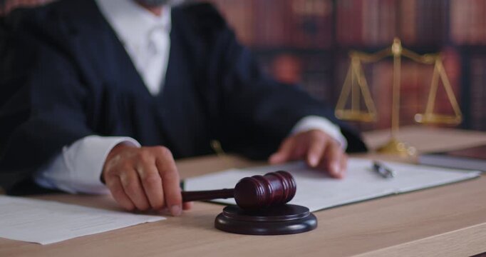 Judge taking gavel in hand to approve courts decision in courtroom. Magistrate delivering justice and law in judgement, sitting at desk with hammer and legal books, documents and scales on hearing