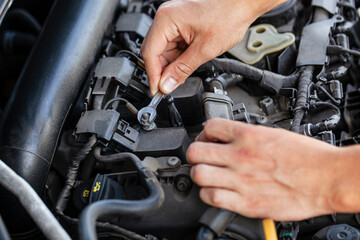 Car engine repair in progress with hands using a wrench to adjust components under the hood