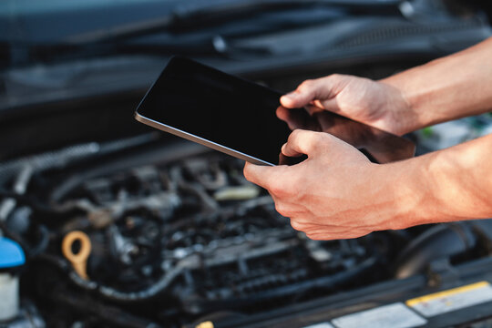 Car maintenance technician using tablet to diagnose engine issues in a workshop