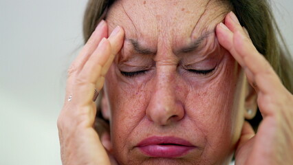 Close-up of senior woman with eyes tightly shut, pressing fingers to temples, intense focus on pain...