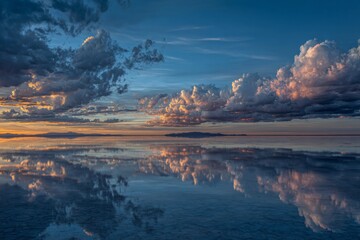 A breathtaking sunset illuminates the expansive salt flat in Bolivia. The tranquil water mirrors the colorful sky and vibrant clouds, creating a surreal landscape