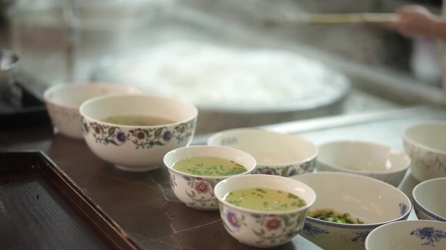 Japanese cuisine with multiple bowls of steaming soup placed on a wooden tray in a kitchen setting