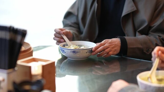 Two people eating from bowls with spoons at a table in a cozy indoor setting