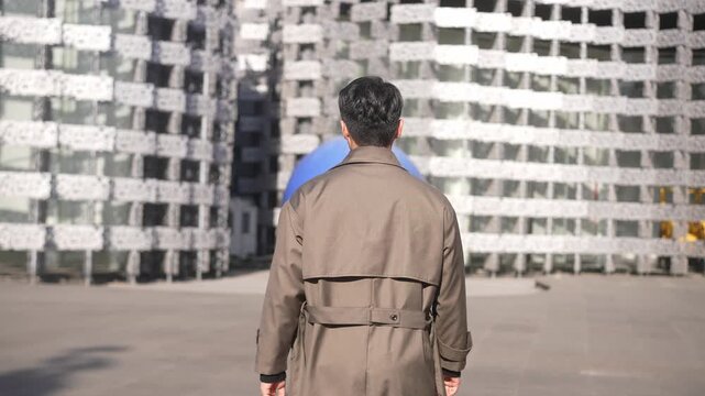 Man in trench coat standing with back to camera in front of modern architectural building