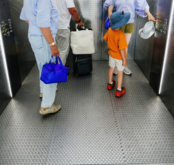 Travelers with luggage and child ride elevator at airport, bright lights and metallic walls create modern transport setting © ifeelstock