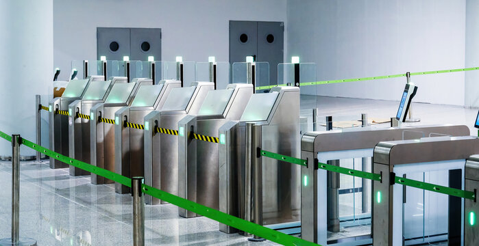 Modern automated passport control gates with glass barriers, scanners, and glowing green lights in empty airport checkpoint hall