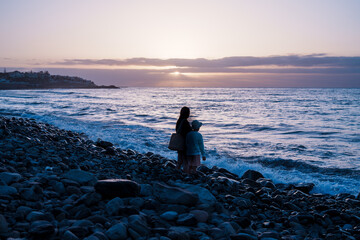 Mother and child admiring stunning ocean sunset on rocky beach © laurentiu