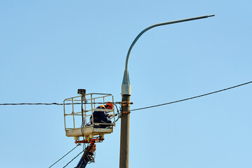 Electrician in safety gear installs new led lamp on tall street light pole from crane bucket,...