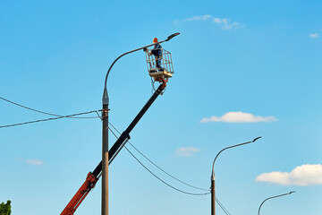 Worker in helmet and safety harness uses crane lift to install led street lamp during outdoor...