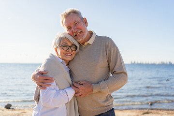 Senior mature couple hugging enjoying outdoor recreation walking on beach. Old husband wife embracing with tenderness love enjoying sweet bonding. Grandmother grandfather together. Family moment love