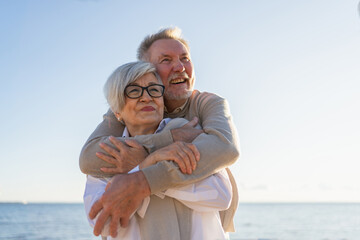 Senior mature couple hugging enjoying outdoor recreation walking on beach. Old husband wife...