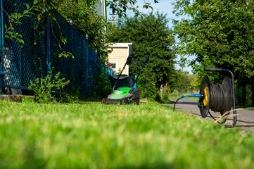 Fototapeta premium Mower sits on freshly cut grass in a residential setting under clear blue skies, with green trees lining the walkway